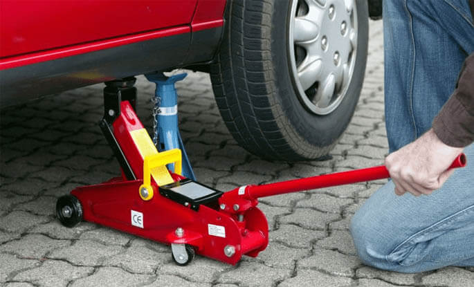 Seseorang sedang memasangkan dongkrak pada mobil
